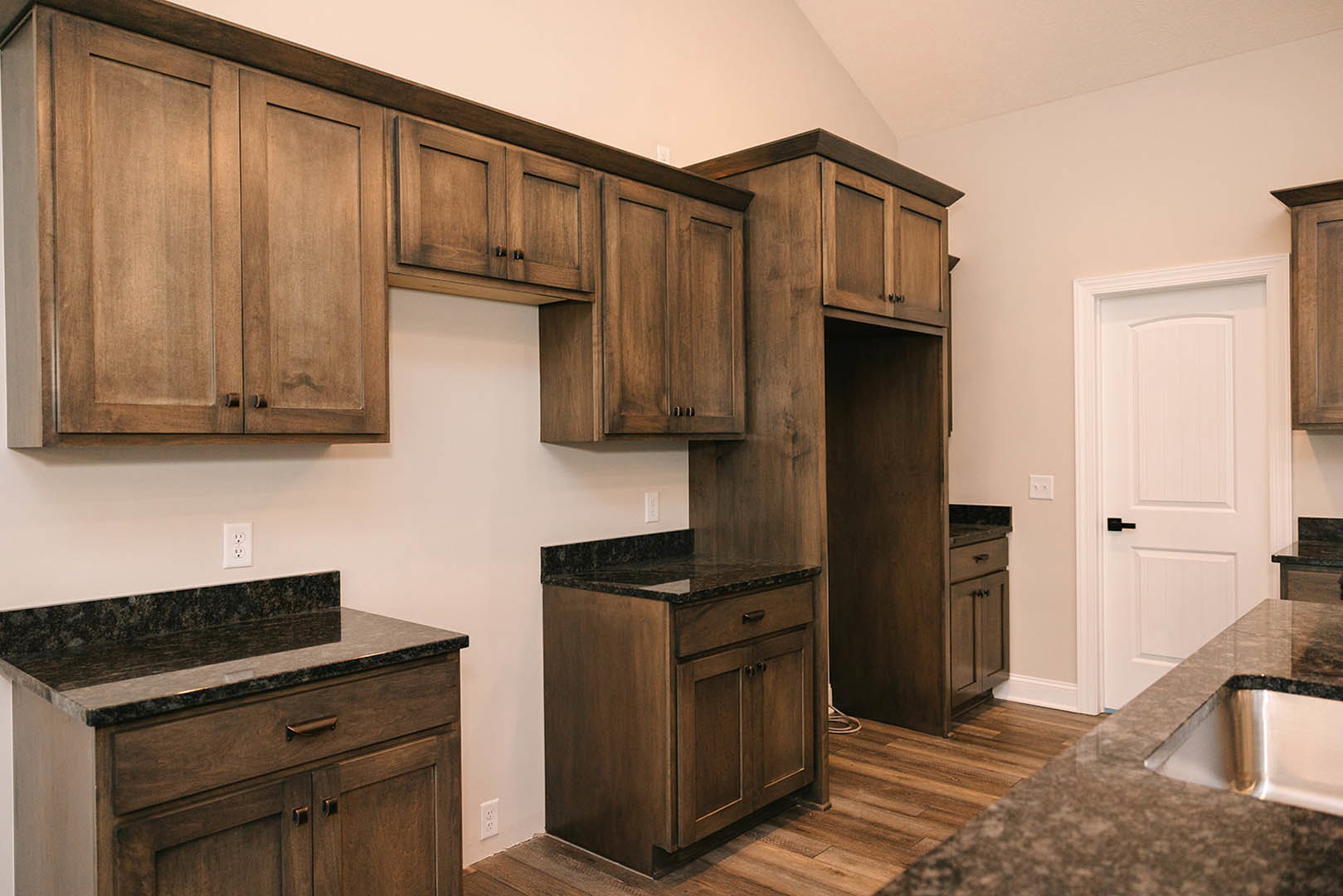 Dark wood kitchen cabinets with marble countertops, stainless steel sink, black hardware, and white door with black handle
