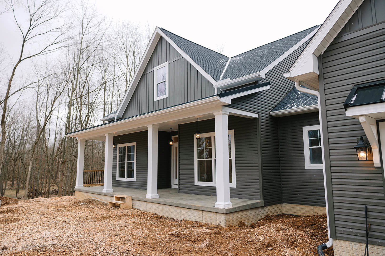 Two-story house with white siding, covered porch featuring white railings and columns, large window with white frame, wooden step stool on porch, mature trees in background