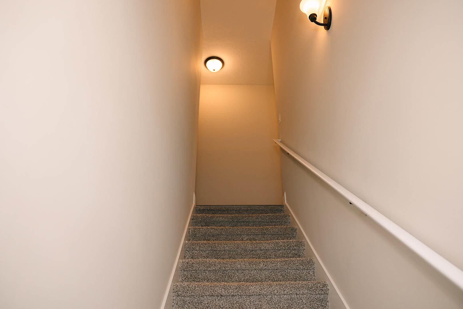 Carpeted staircase with modern ceiling light fixture, plaster walls, and soft lighting illuminating the landing