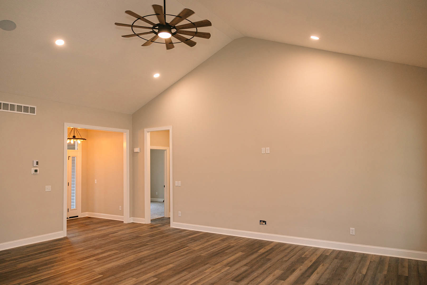 Ceiling fan with integrated light above hardwood flooring and white baseboards, neutral walls, partial view of door and ceiling fixture.