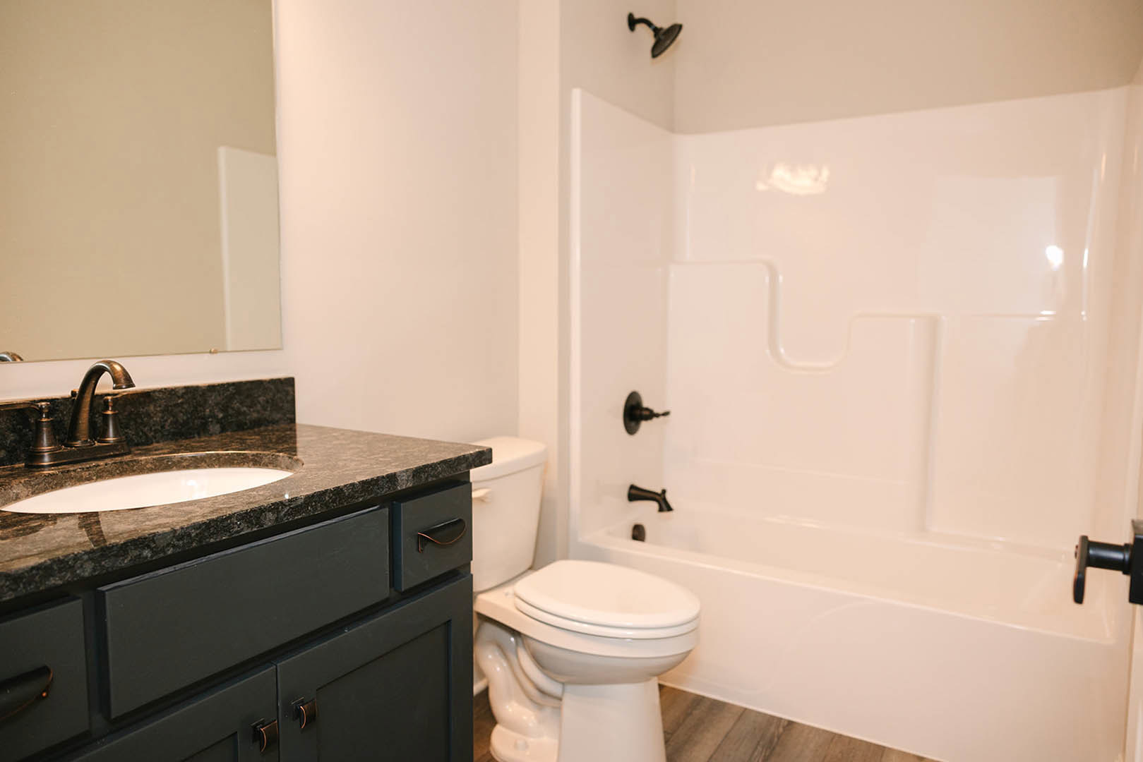 Modern bathroom with white bathtub, wall-mounted sink on a stone countertop, chrome faucet, black cabinet handle, and tiled walls