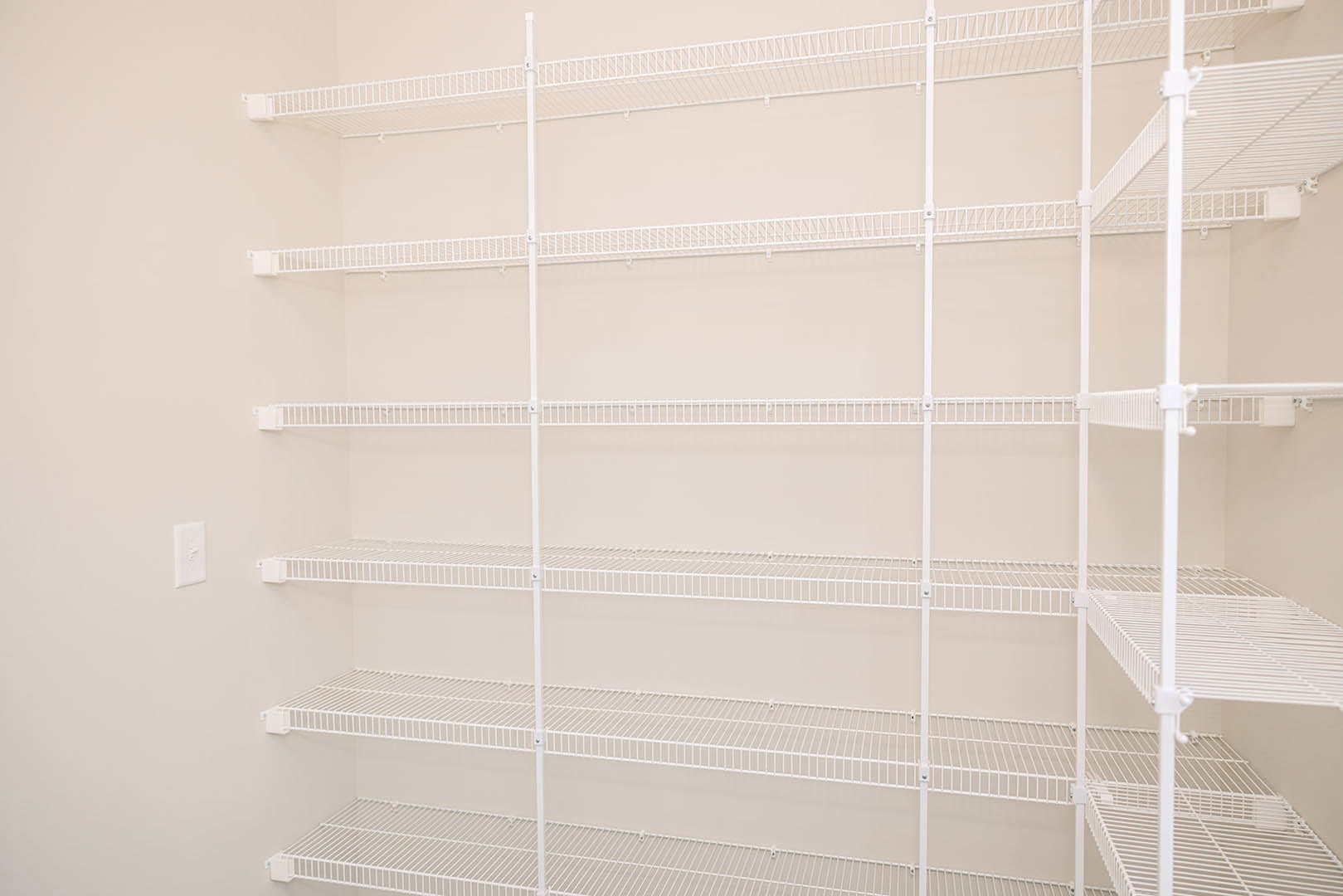 White built-in shelves mounted on a smooth white wall beside a window with sheer white curtains, displaying minimalist design in a bright indoor room.