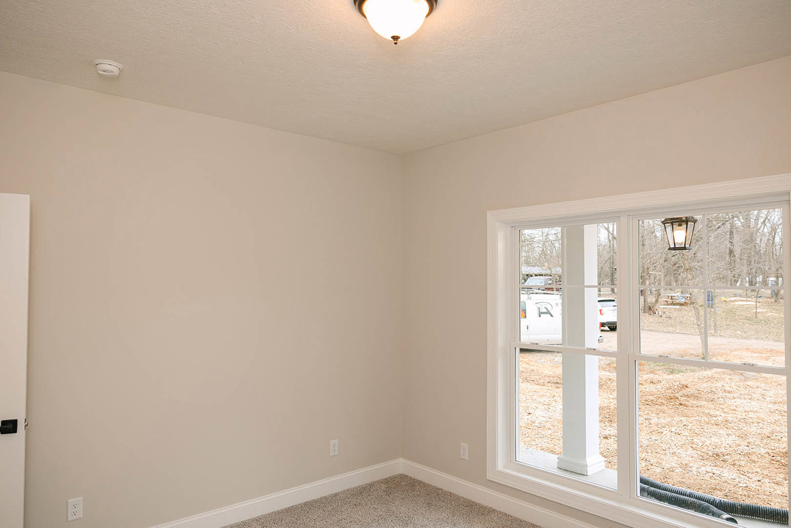 Carpeted room with white plaster walls, window with blinds, round ceiling light fixture, and smoke detector on ceiling