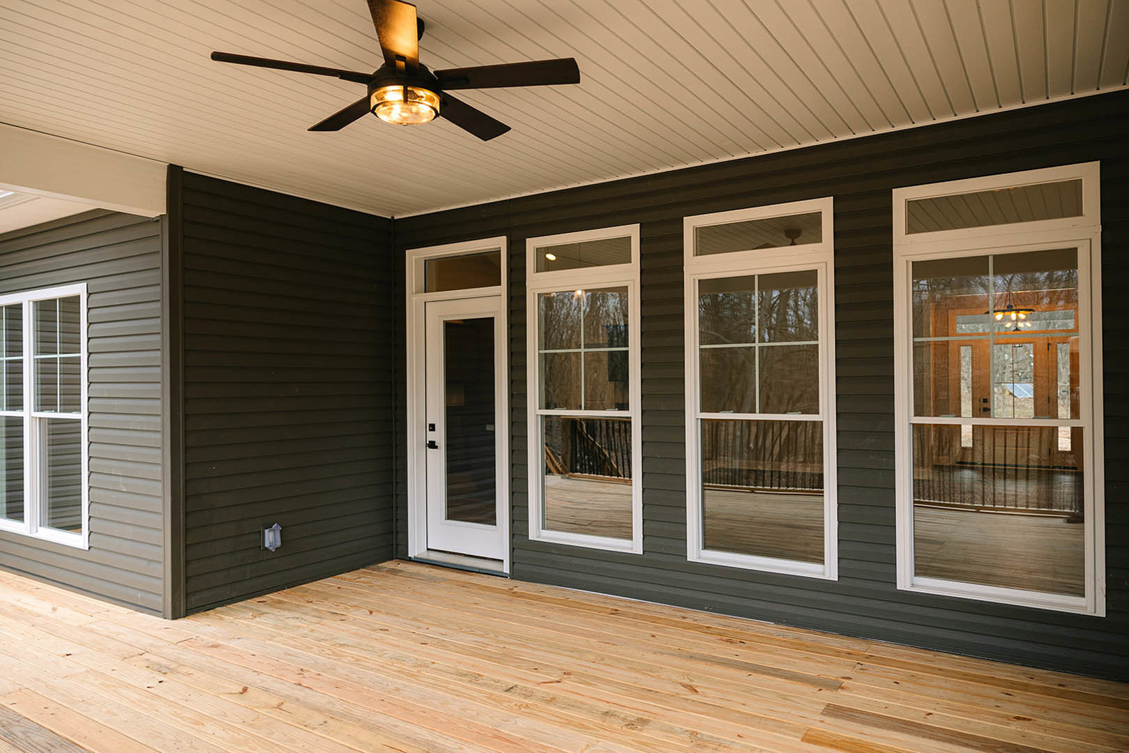 Ceiling fan with light above wooden porch floor, glass door and white-framed window on exterior wall