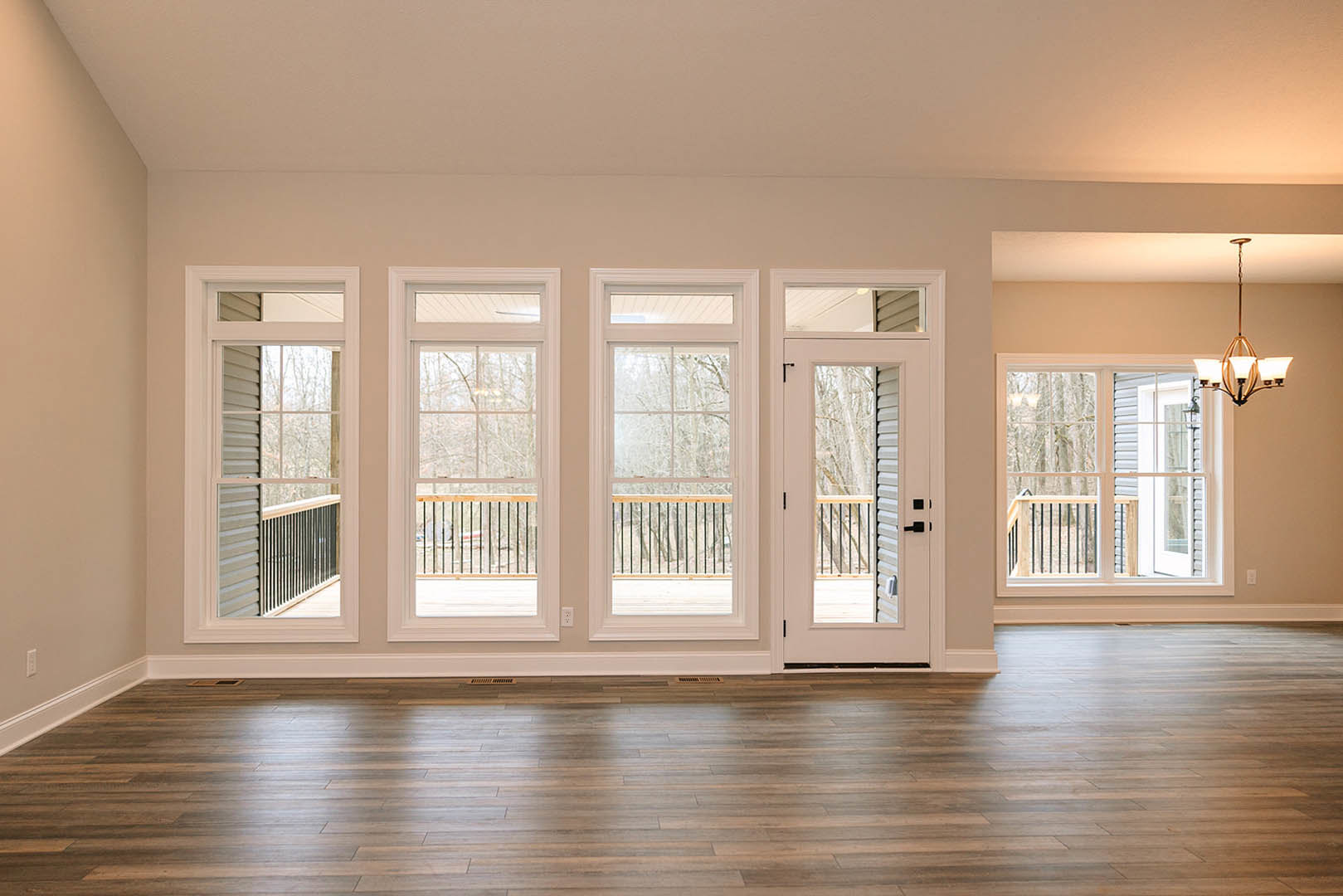 Hardwood flooring in a spacious room with white walls, multiple large windows, and a modern chandelier