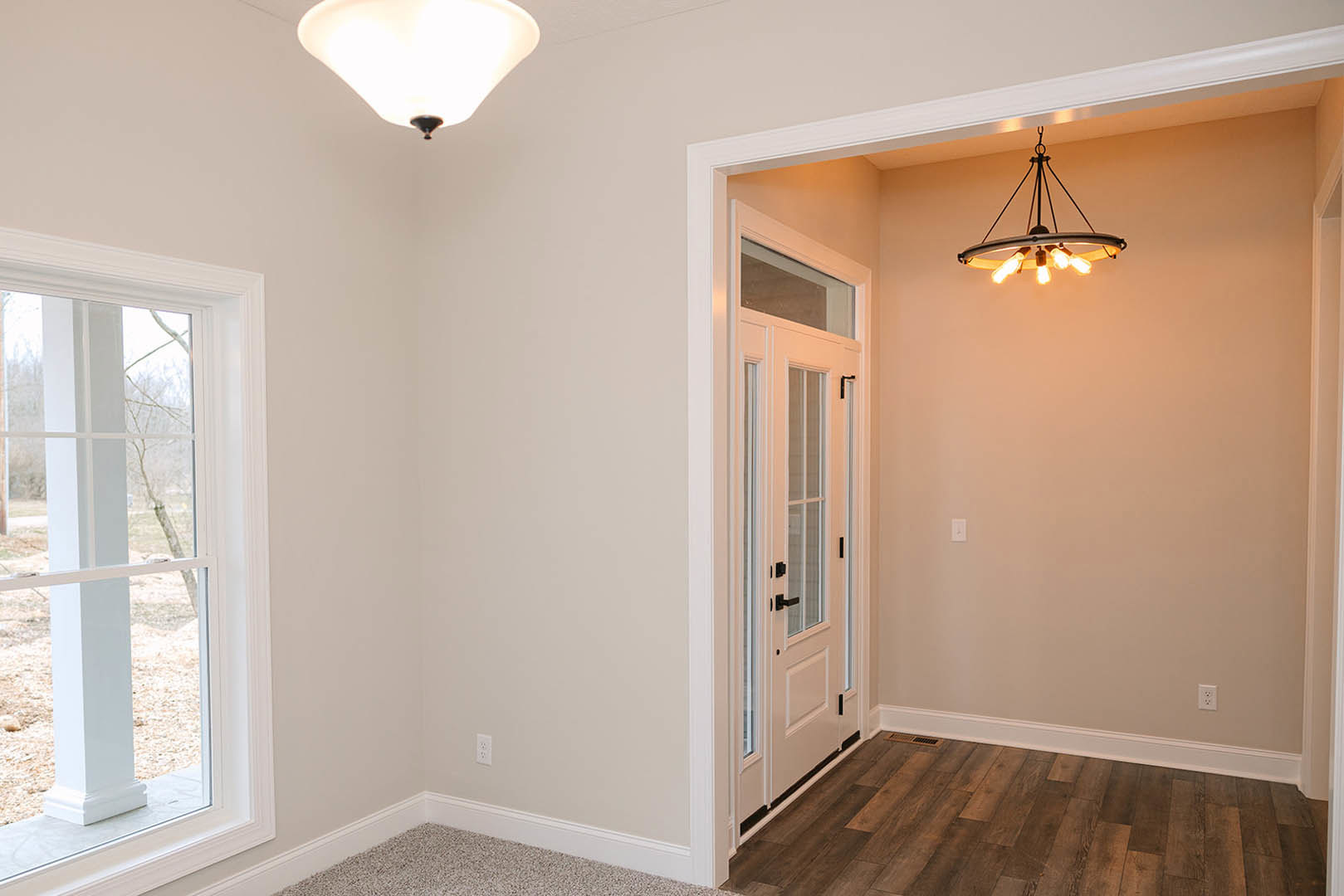 Hallway with wood flooring and white trim, ceiling-mounted light fixture, white door, window showing tree outside