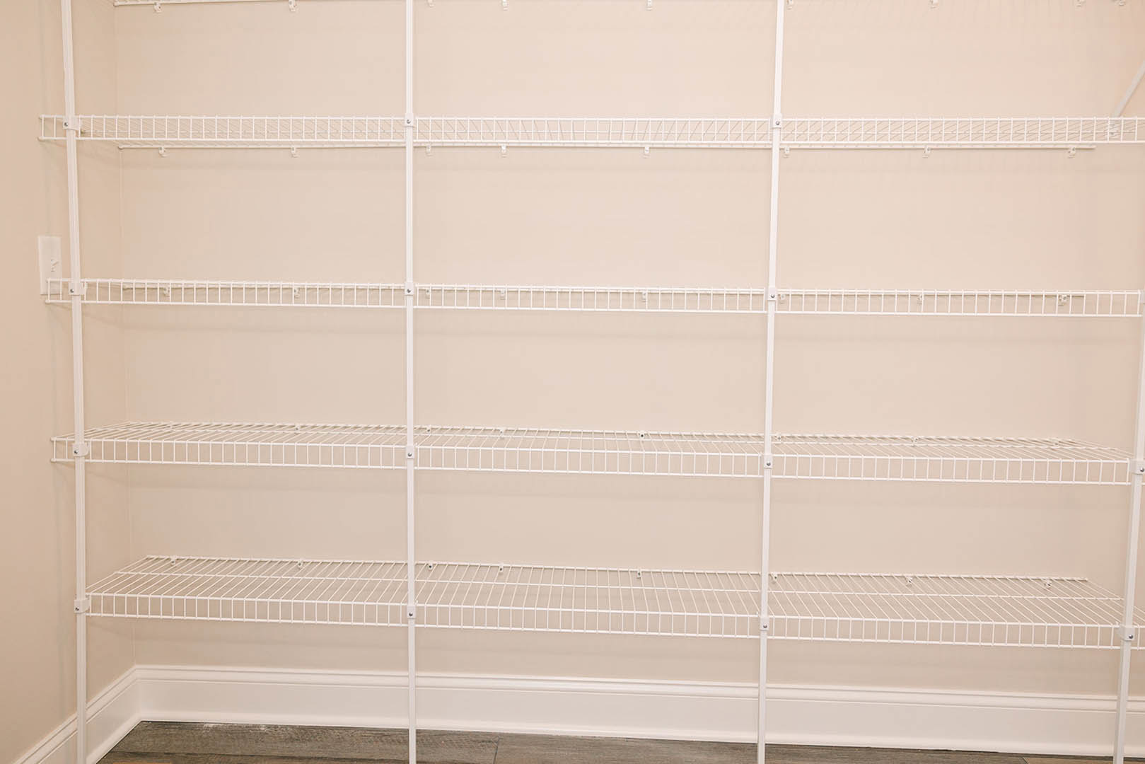 White wire shelving unit mounted on a white wall with matching baseboard in a residential room