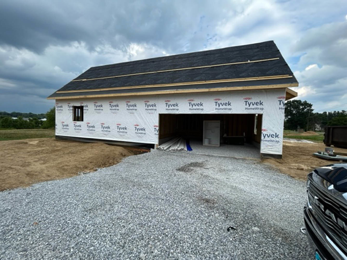 Partially built house with white sheathing, black trim, gravel driveway, and black pickup truck parked in front