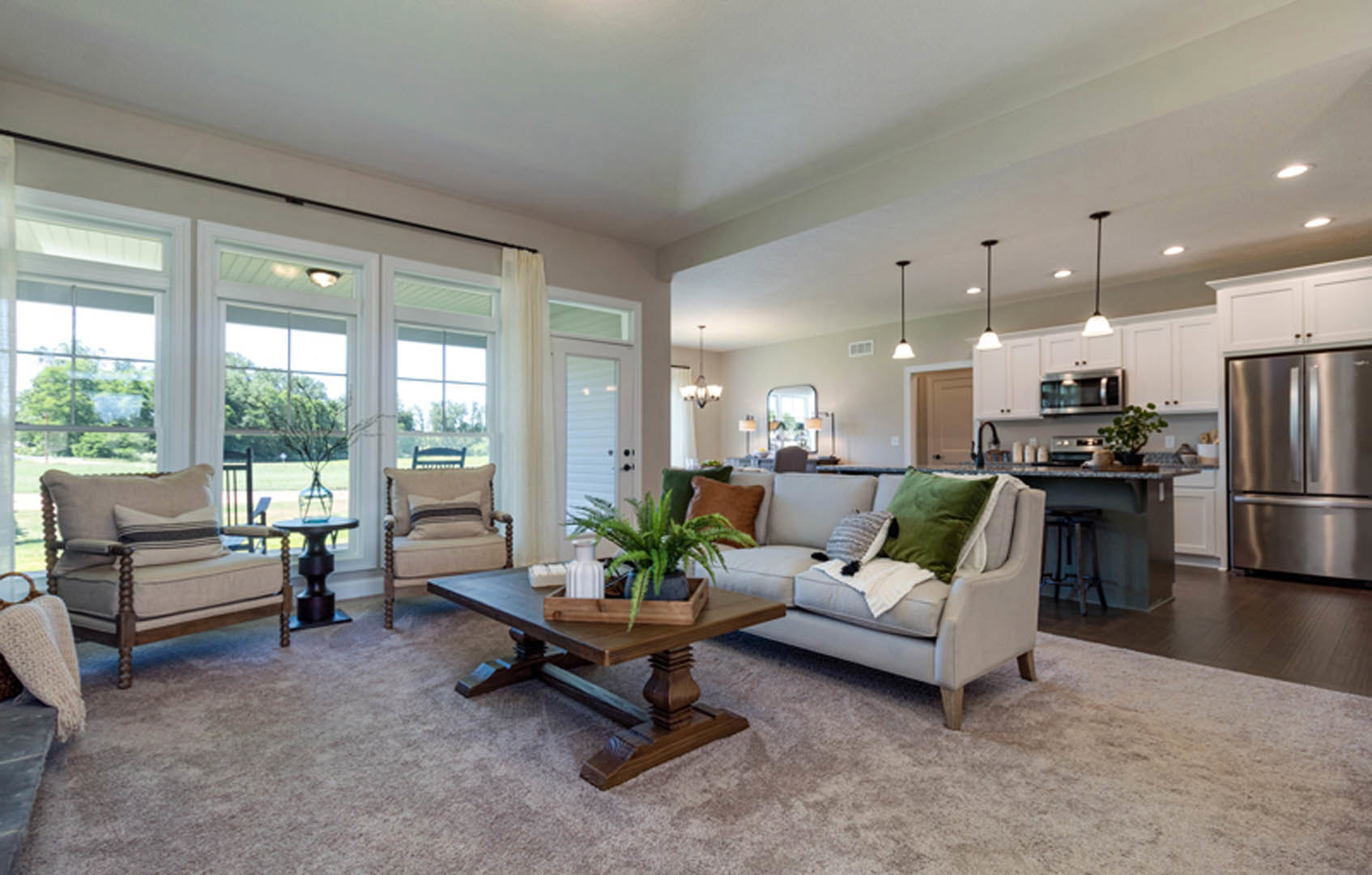 Living room with light-colored couch, decorative pillows, wooden coffee table topped with potted plant, neutral walls, hardwood flooring, and stainless steel refrigerator visible