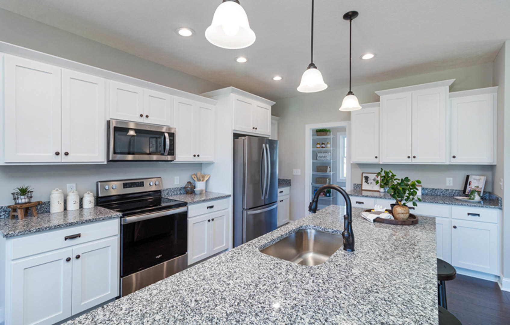 Granite countertops, stainless steel appliances including microwave, refrigerator, stove, white cabinetry, undermount sink, potted plant on counter