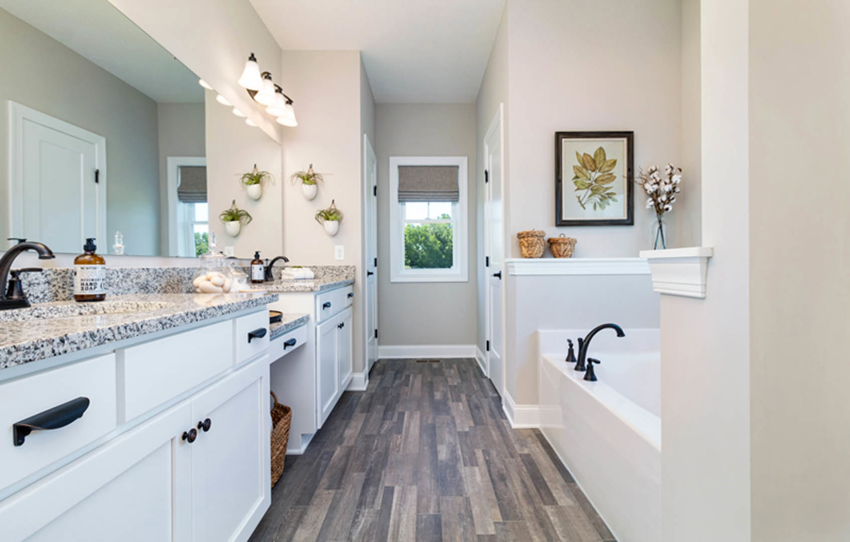 Bathroom with marble countertops, freestanding tub, wood flooring, potted plant, window with fabric shade, and modern fixtures