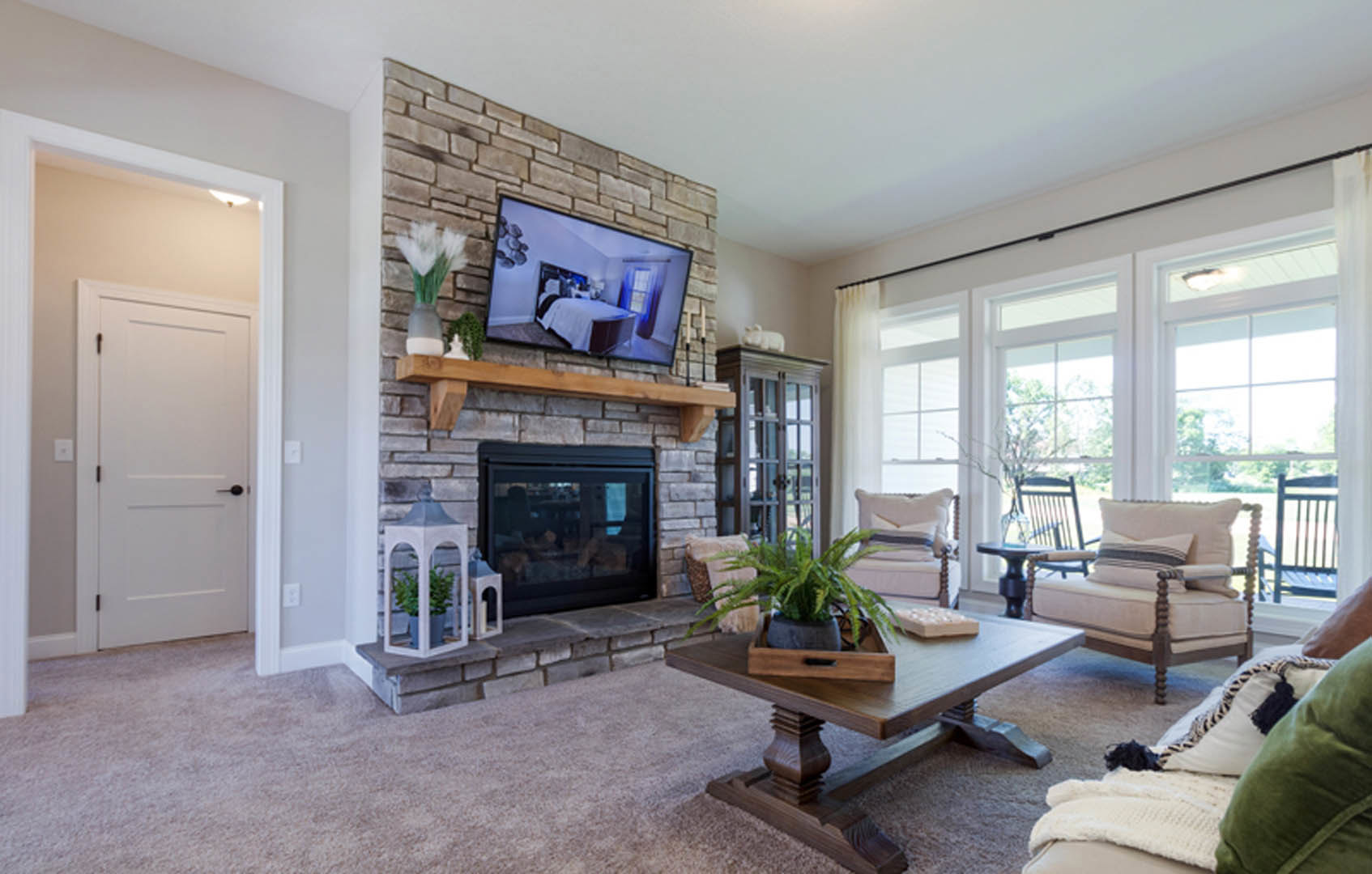 Living room with brick accent wall featuring mounted television and glass-door fireplace, wooden coffee table with potted plant, upholstered chair, white door with black handle