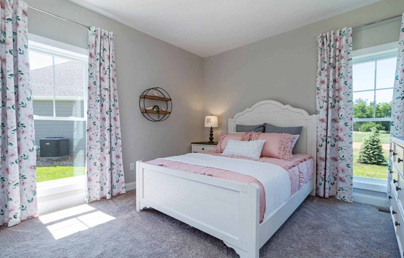 Queen bed with pink and white pillows, white bedding, sheer curtains, wall-mounted shelf displaying a decorative bird, neutral walls, and soft natural light.