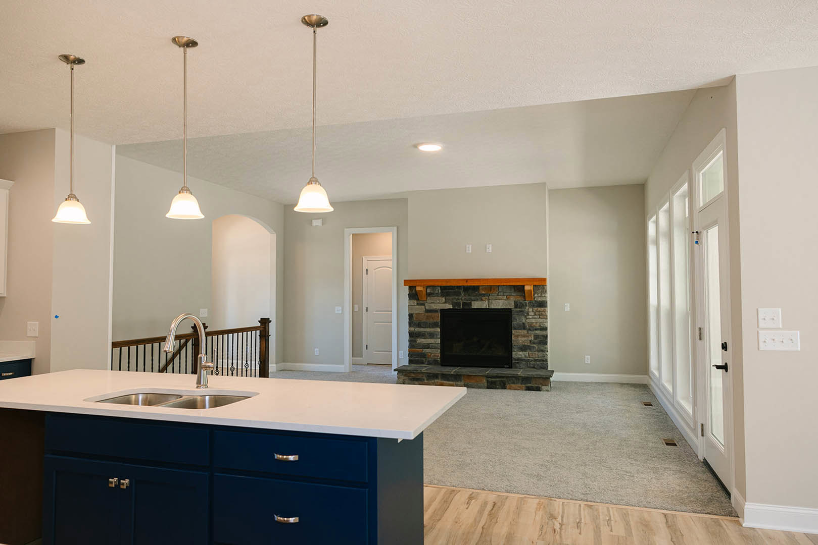Modern kitchen featuring a central fireplace with a black screen, white cabinetry, stone countertops, stainless steel sink, wood flooring, and a wall-mounted light fixture.