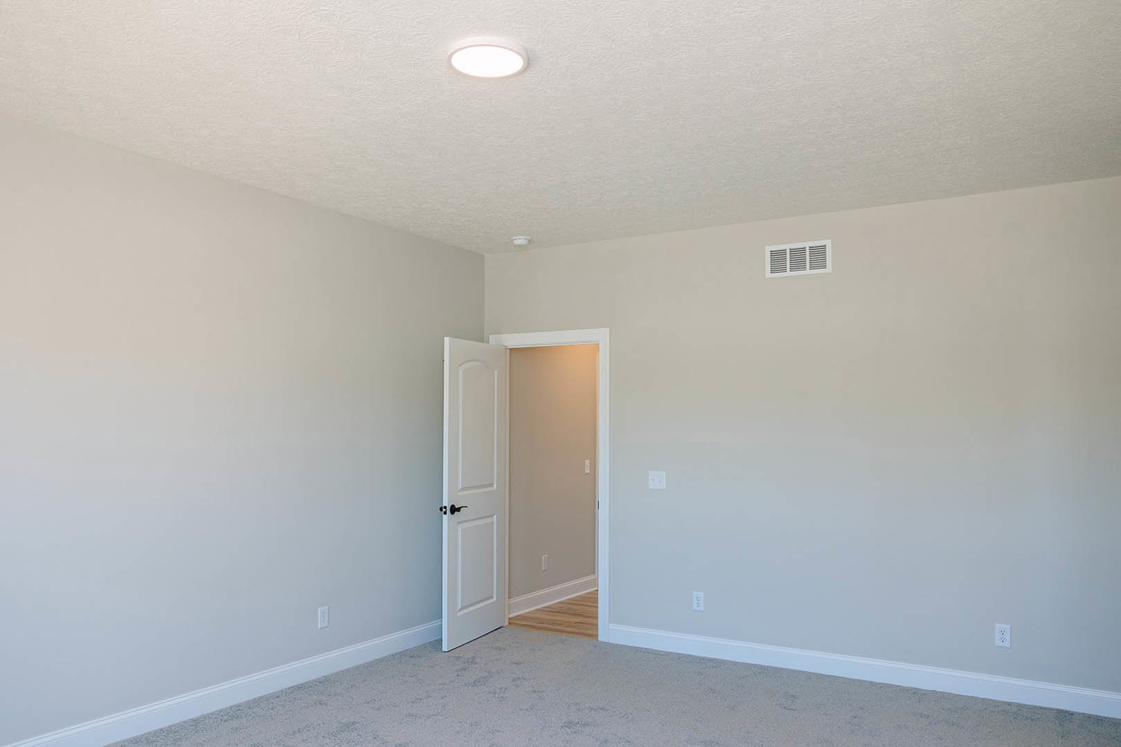 White paneled door open to carpeted room with white walls, ceiling vent, recessed light, and simple baseboards