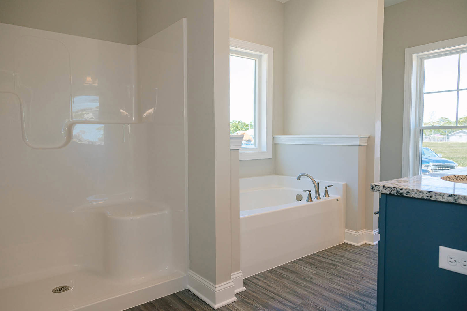Bathroom with freestanding white bathtub beneath a large window, light gray tile walls, chrome faucet, and natural light illuminating the space