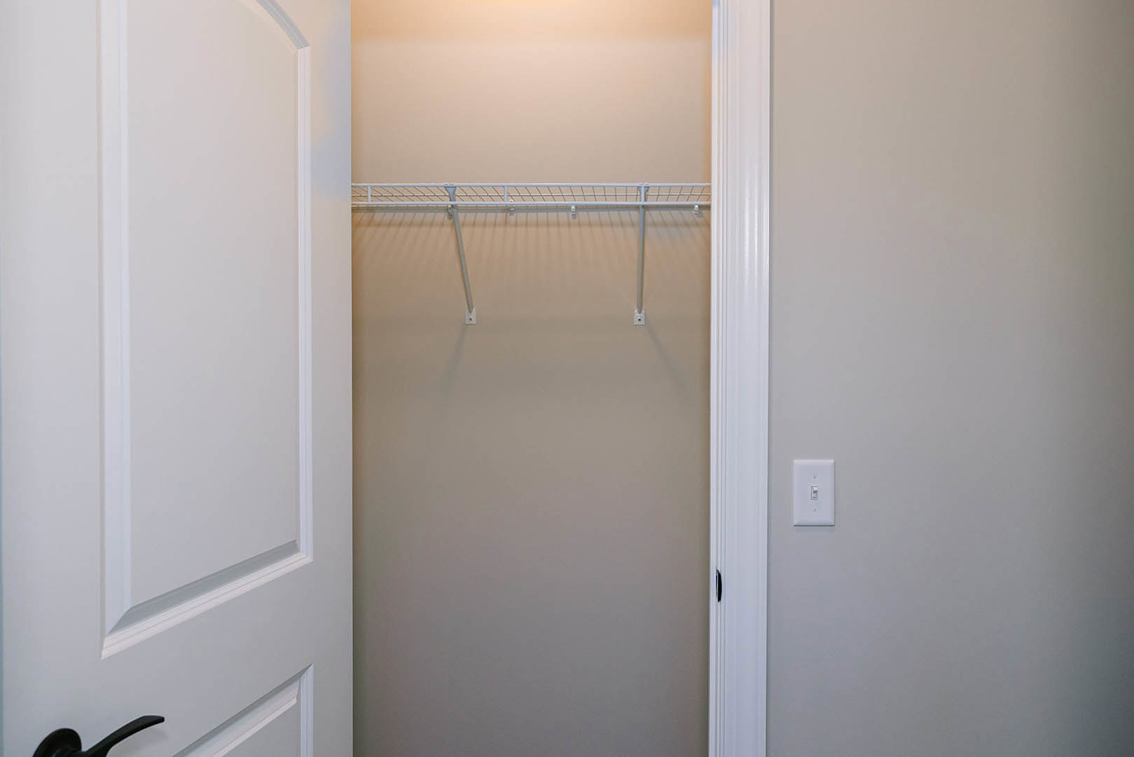 White closet with built-in shelf, white walls, white door, light switch, and curtain rod visible.
