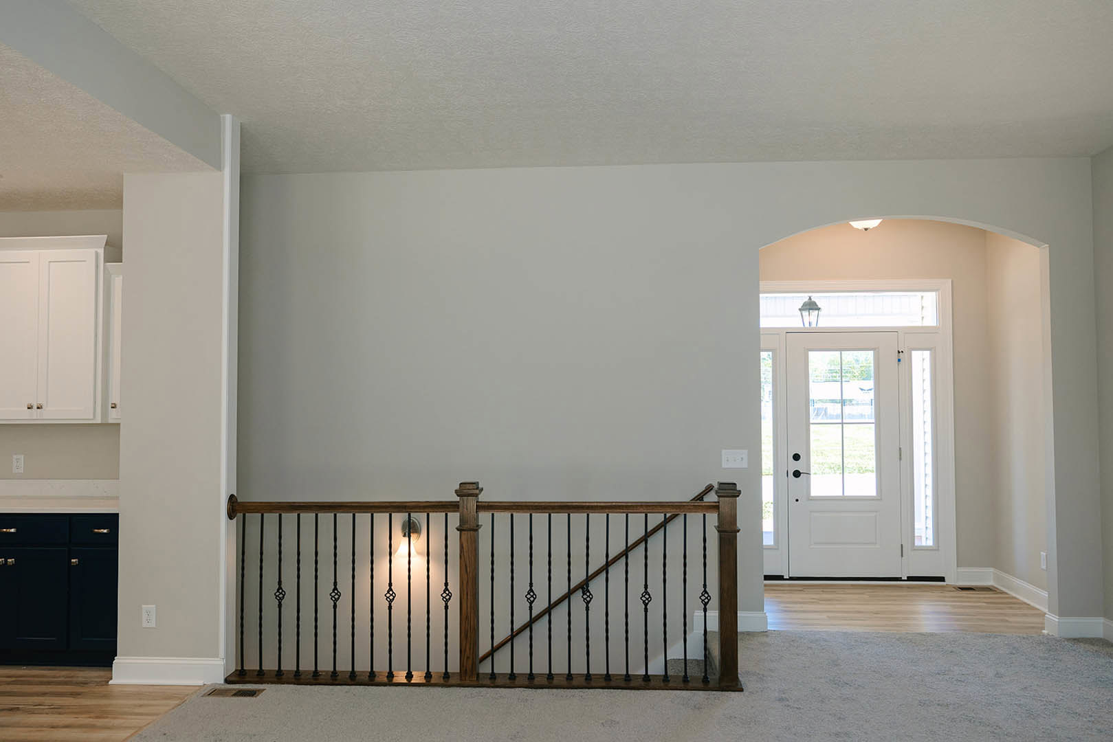 Wood staircase with white risers and dark railing, glass-paneled white door, black cabinet, and light grey walls in a modern home interior