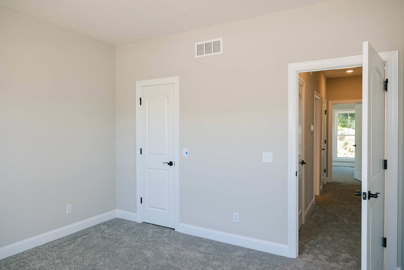 White carpeted room with white paneled doors featuring black handles, white walls, wall outlet, and air vent.