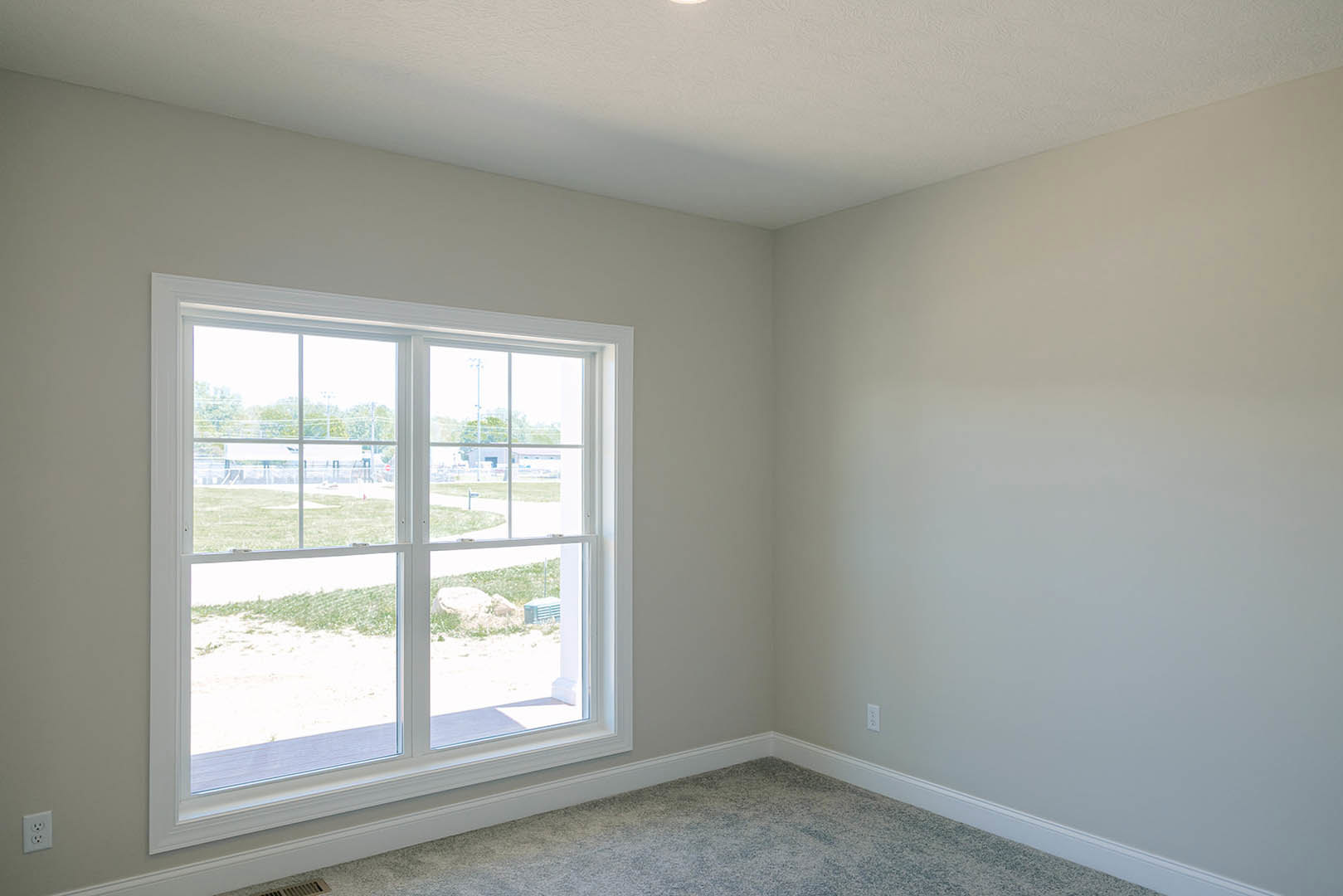 Bright room with white walls, large window overlooking grassy field, beige carpet flooring, simple window blind
