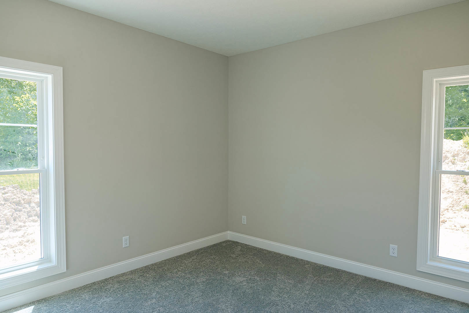 Corner of a carpeted room with white walls, large window framing a view of the Rocky Mountains and cloudy sky