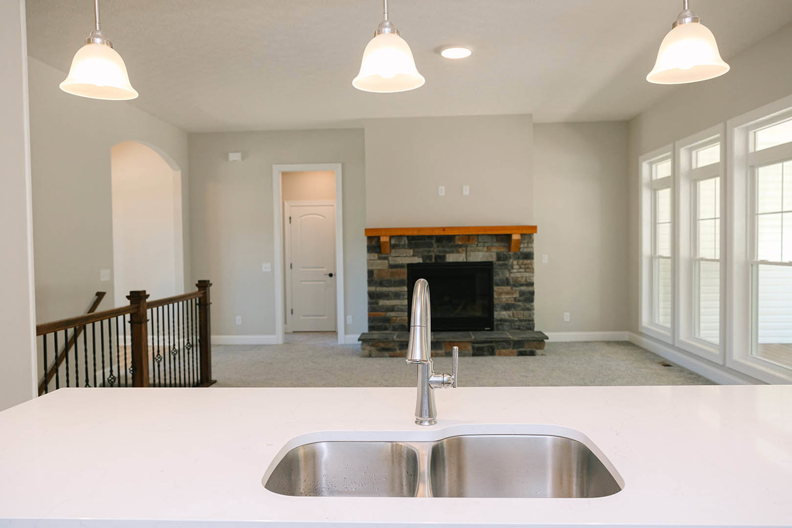 Quartz countertop with stainless steel sink and modern faucet, white cabinetry, and stone fireplace visible in the background
