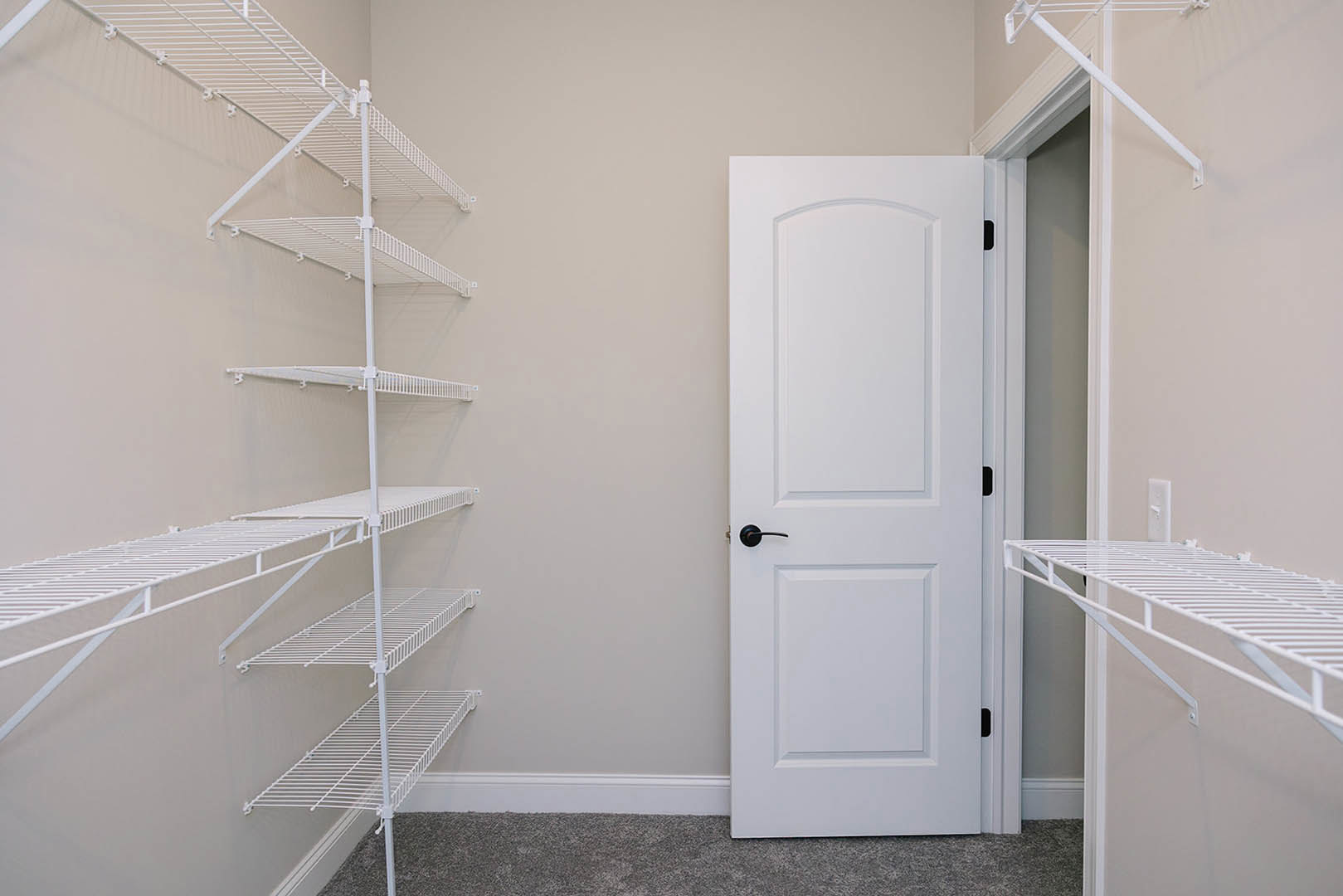 White paneled door with black handle beside built-in white shelves on plaster wall in bathroom.