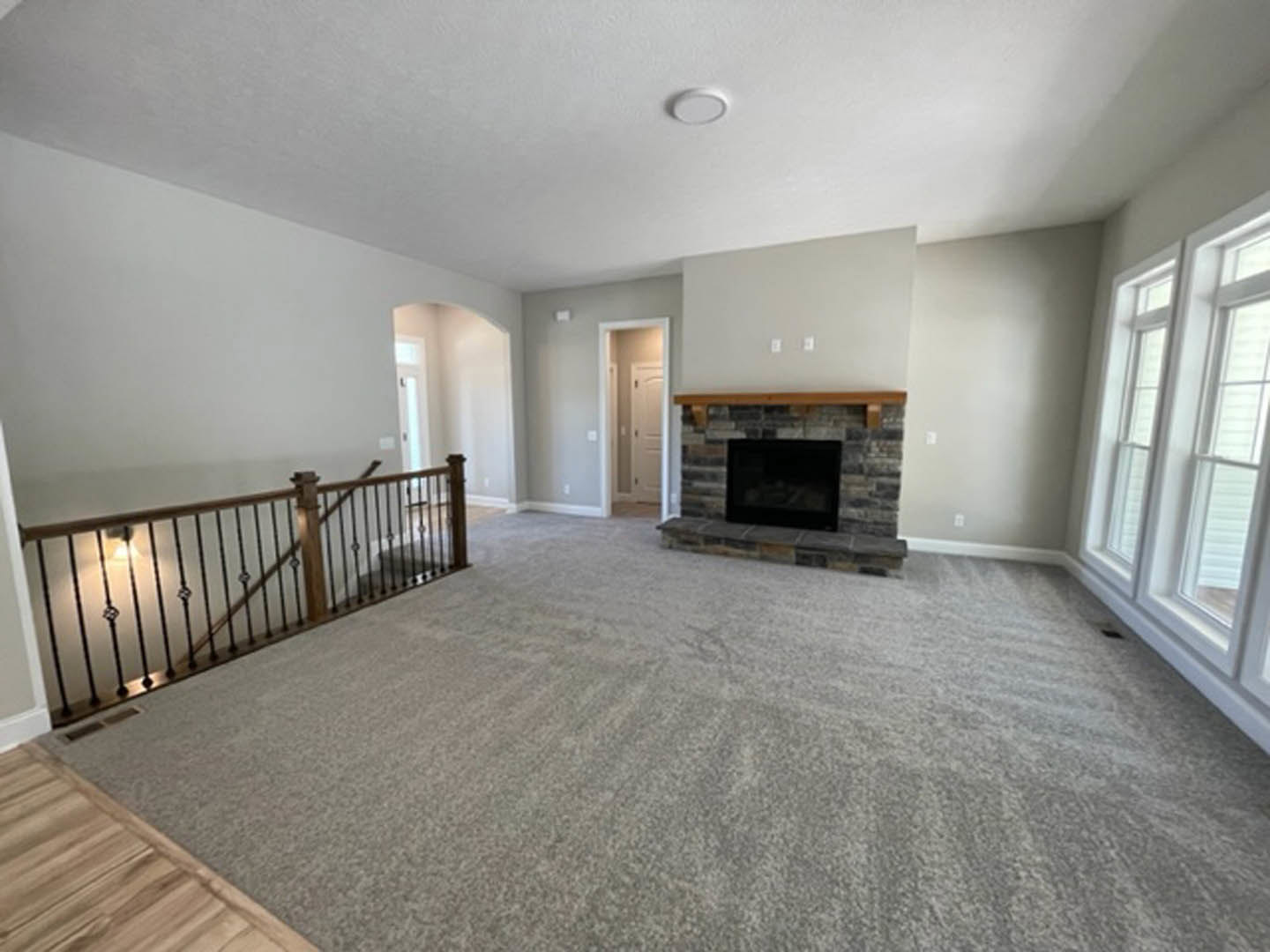 Living room with carpet flooring, white walls, modern fireplace with glass front, wood staircase featuring a railing, and laminate flooring near the entry.