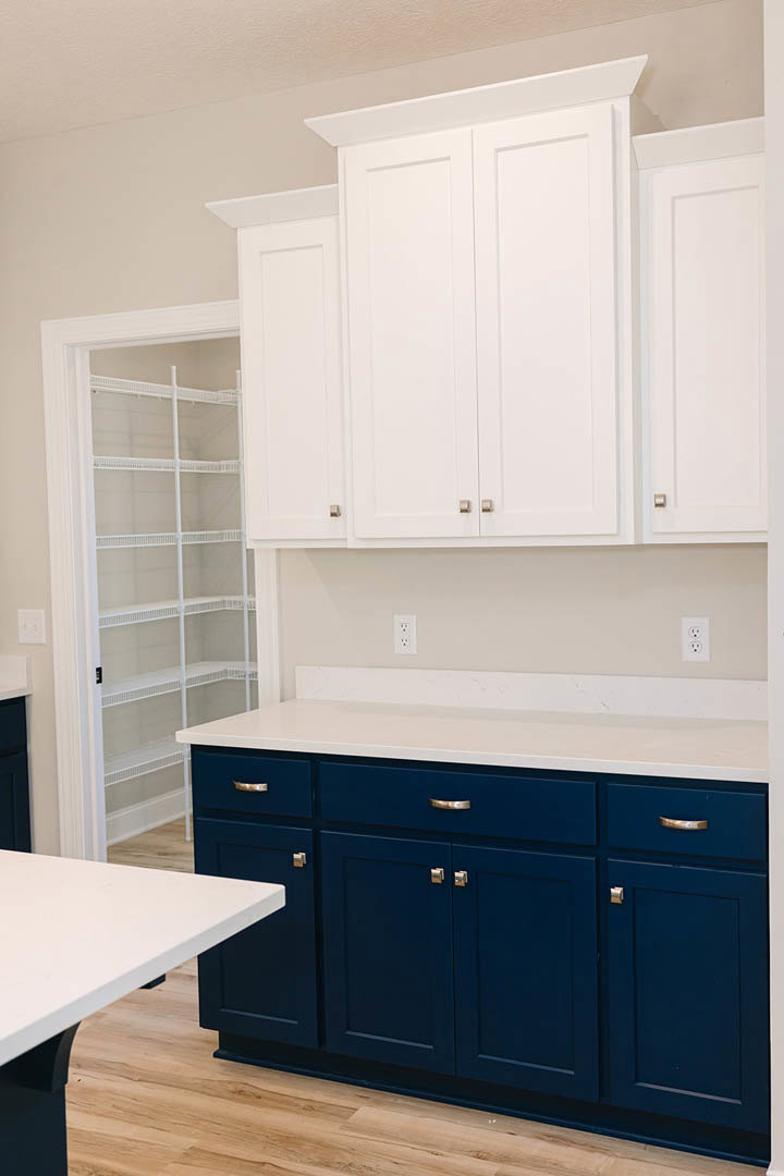 Blue kitchen cabinets with silver handles, white countertops, stainless steel sink, and white open shelving against a light-colored wall