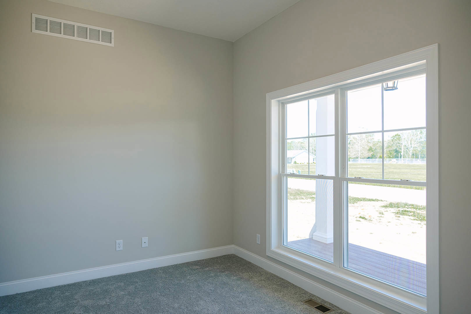 Sunlit room with white plaster ceiling, large window with blinds, neutral carpet flooring, and floor vent near the wall.