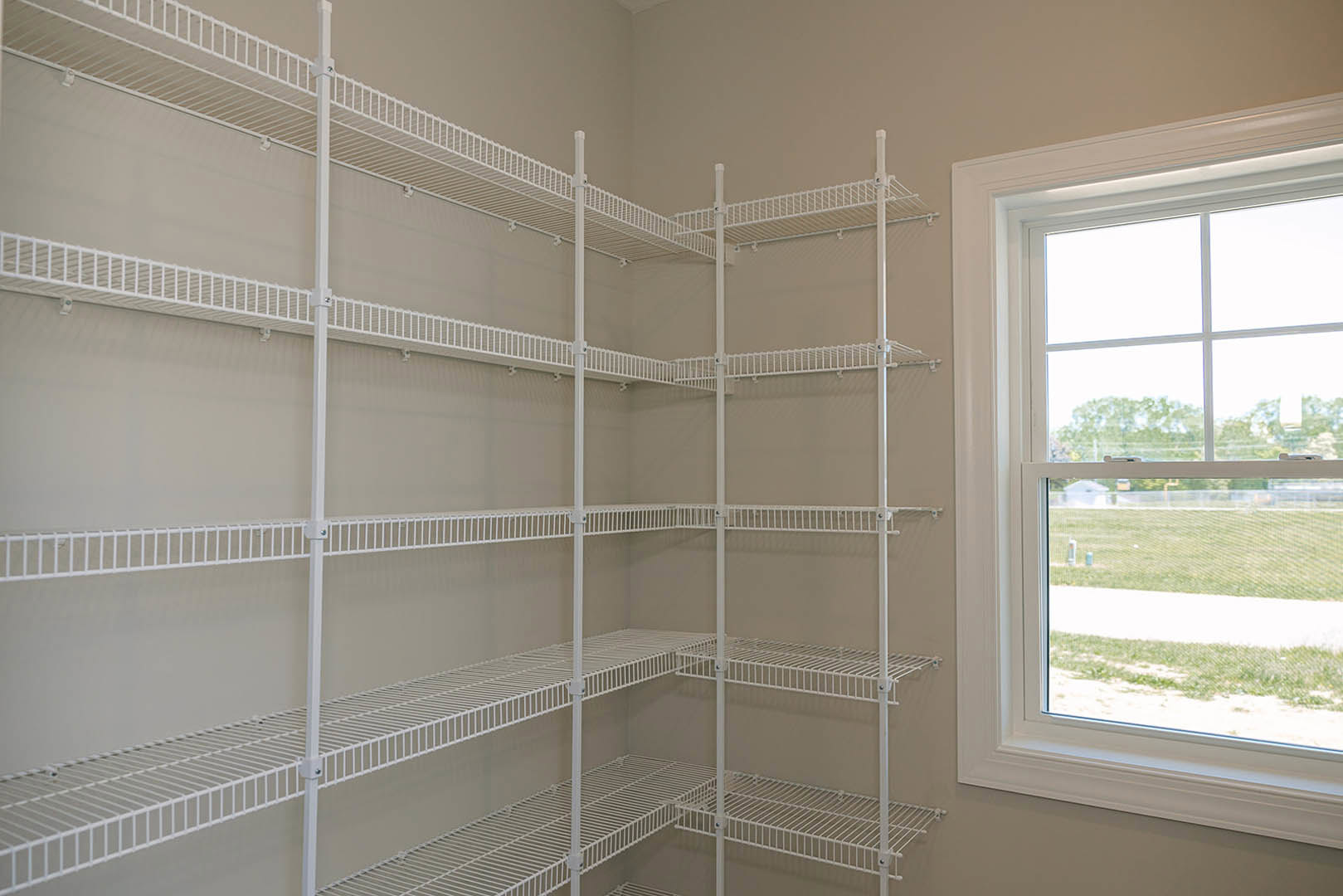 White wire shelving mounted on a wall beside a window overlooking a grassy field in a bathroom.