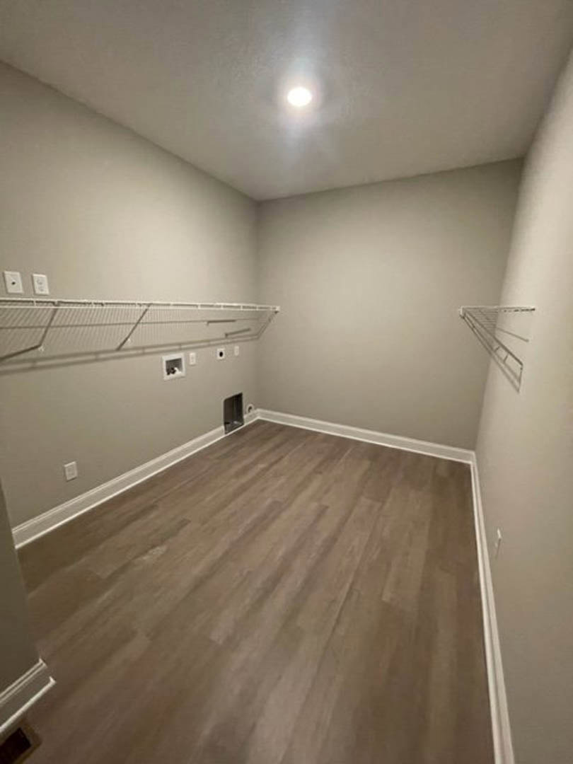 Wood flooring in a room with white shelving mounted on a plaster wall, metal bar and net accents, plywood ceiling