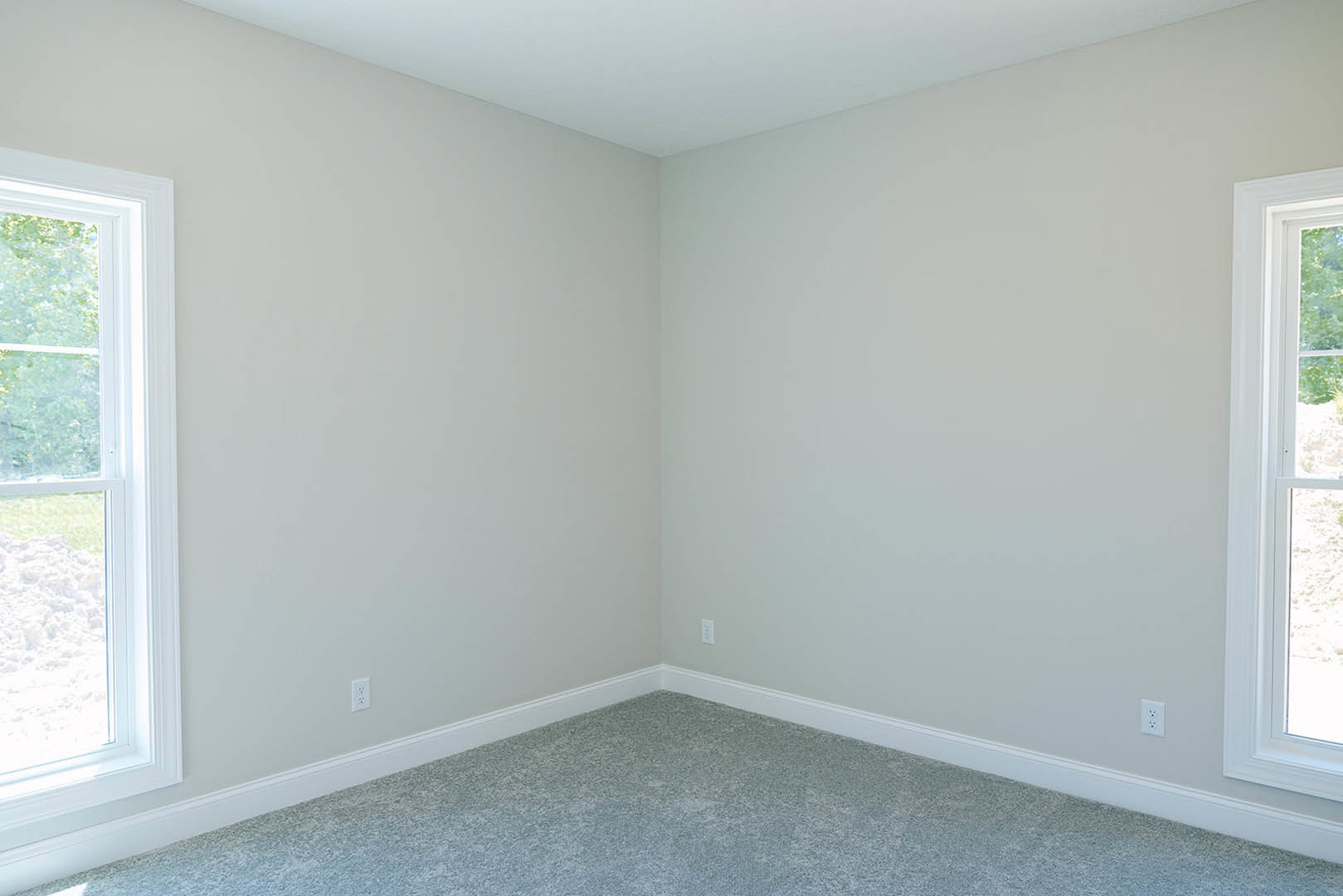 Corner of a carpeted room with white walls, large window, and simple ceiling molding