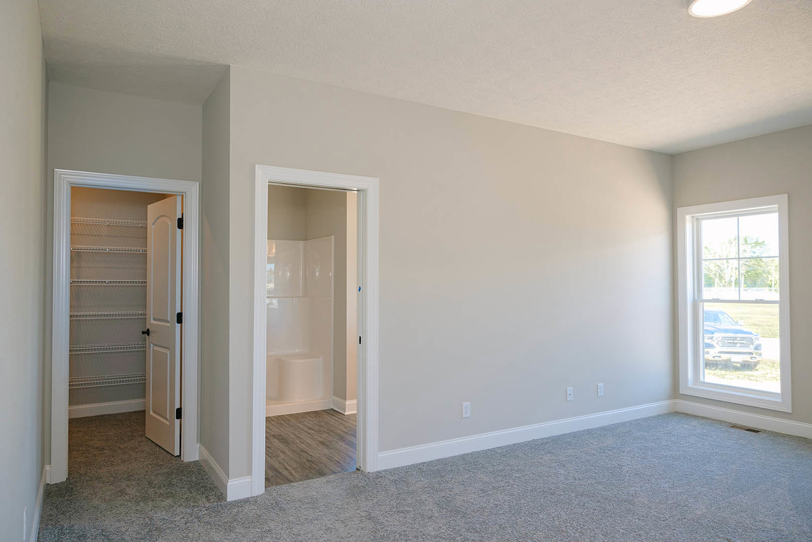 Bathroom with white tile shower featuring a step, open door leading to adjacent room, built-in closet with open shelving, window showing parked car outside
