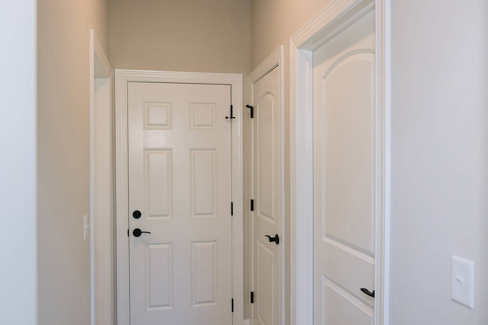 White hallway with white door featuring black handle, white door frame, and smooth white walls