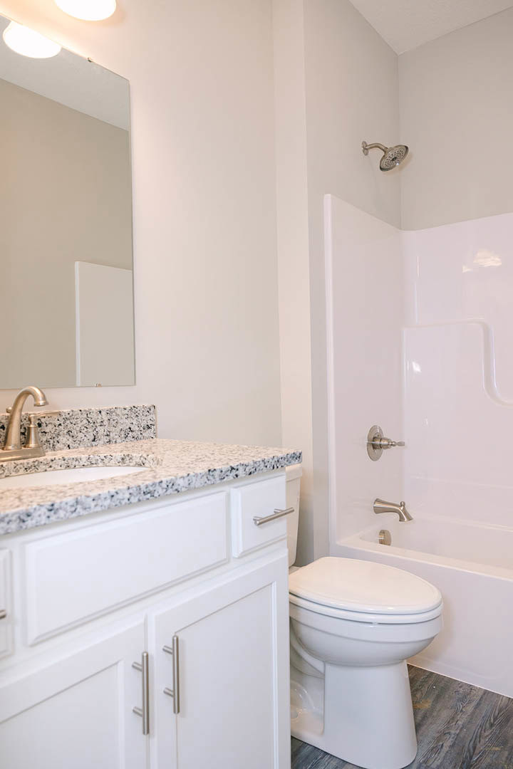 Modern bathroom featuring a tiled walk-in shower with chrome showerhead, white vanity with integrated sink and sleek faucet, white toilet, and minimalist white walls with matching