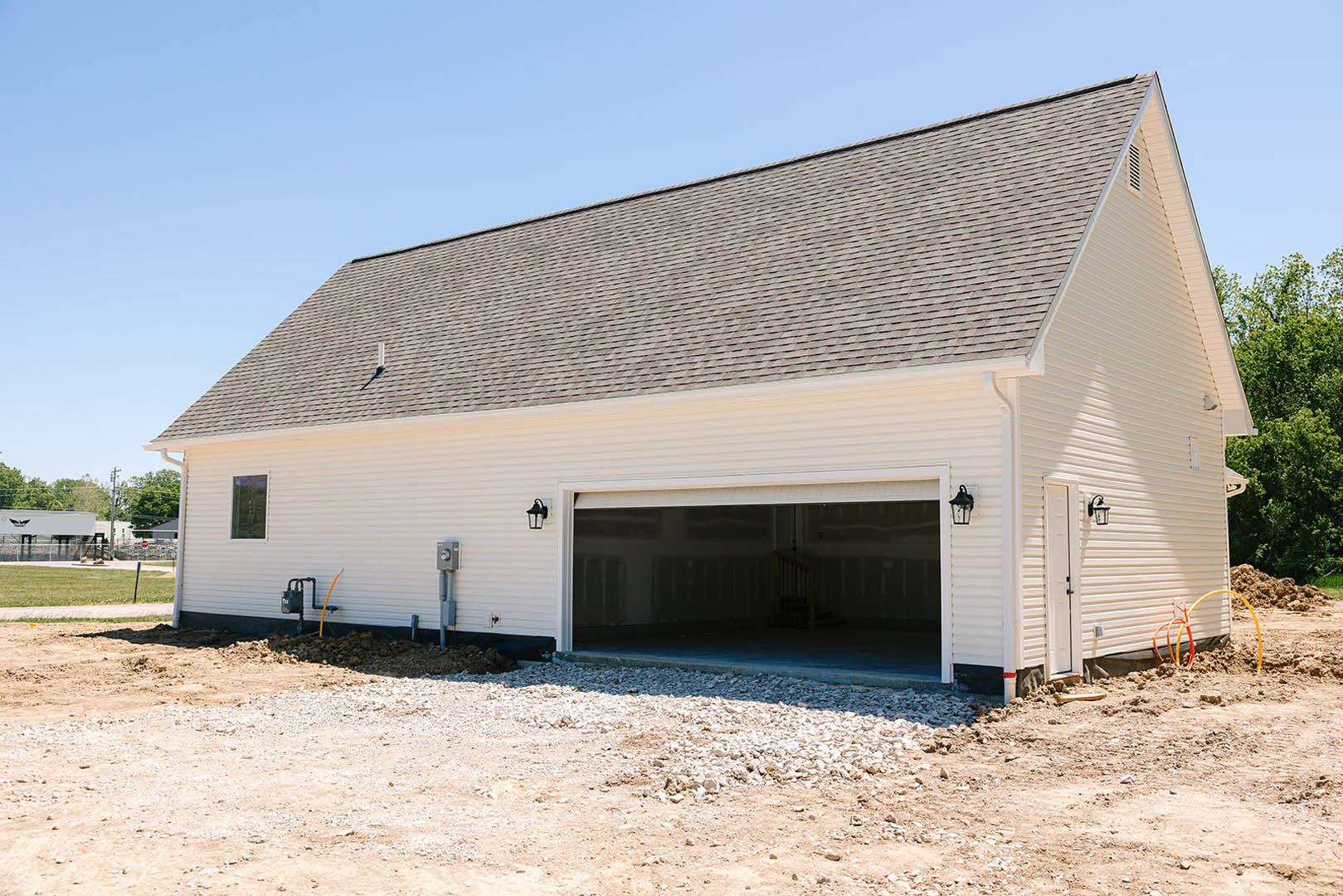 White modern house exterior with attached garage featuring a large gray door, white siding, visible staircase, black utility box with pipes, yellow and orange tubing along the