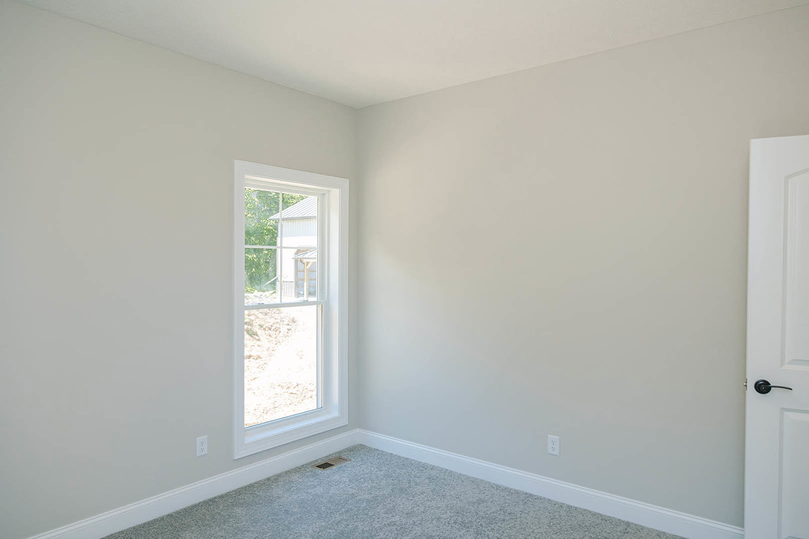 Carpeted room featuring a white framed window, white door, wall vent, and smooth plaster walls.