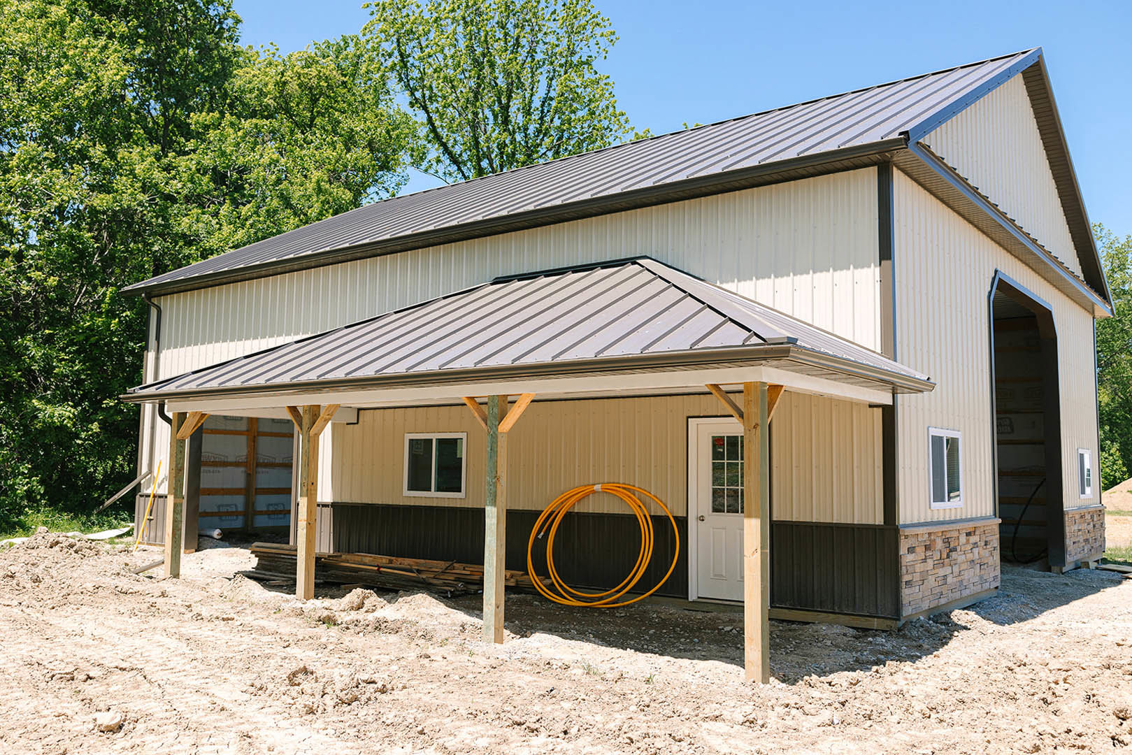 Covered porch with white framed windows, white door, yellow pipes mounted on exterior wall, metal hoop near roof, surrounded by trees and sky.