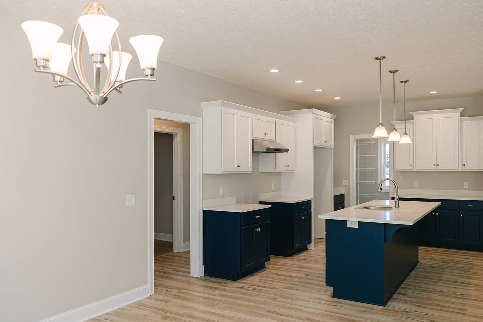 White kitchen cabinets, blue island with white countertop and built-in sink, modern chandelier overhead, stainless steel faucet, hardwood flooring, and recessed ceiling lighting.