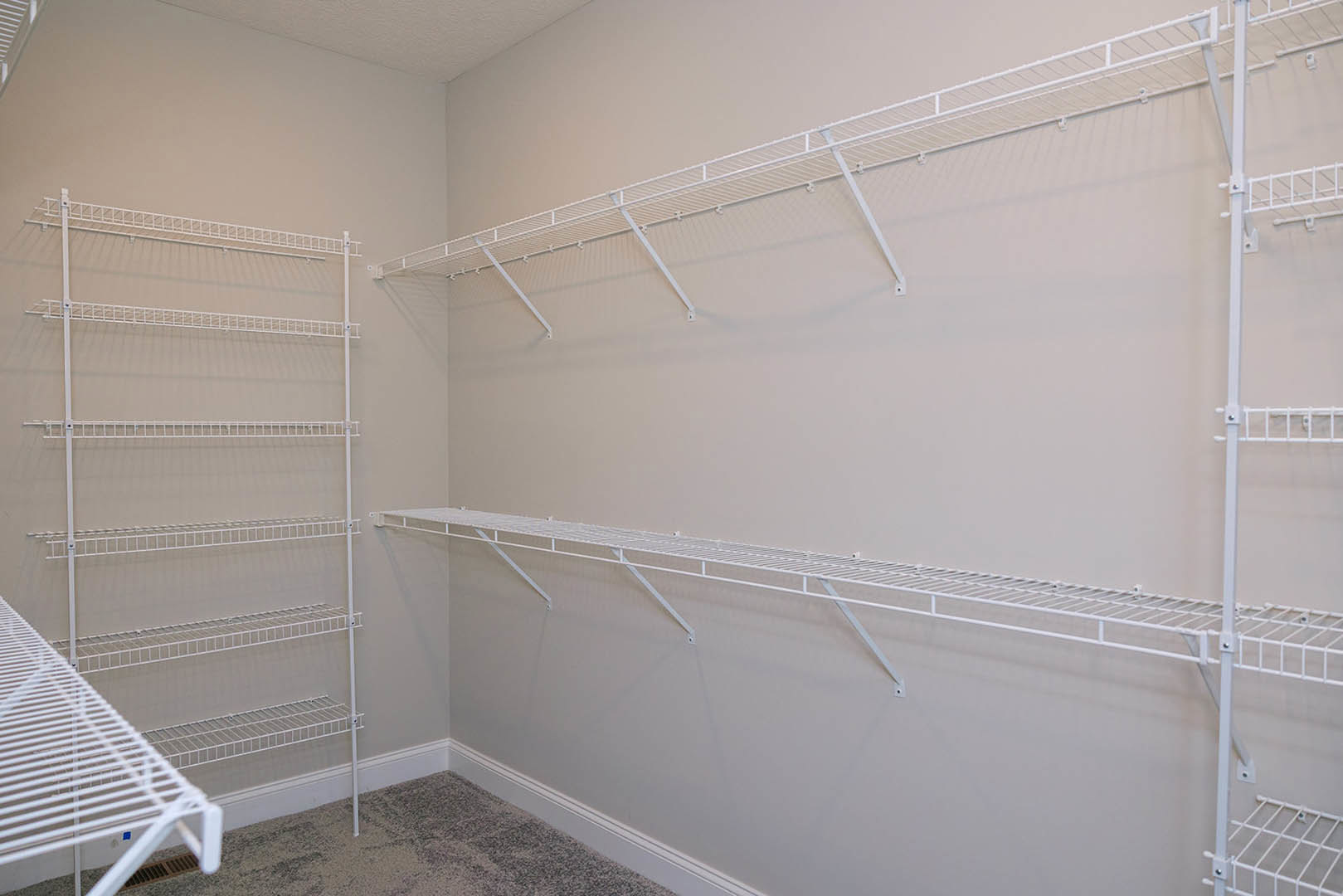 White built-in shelves mounted on a plaster wall, with a carpeted floor visible in the foreground.