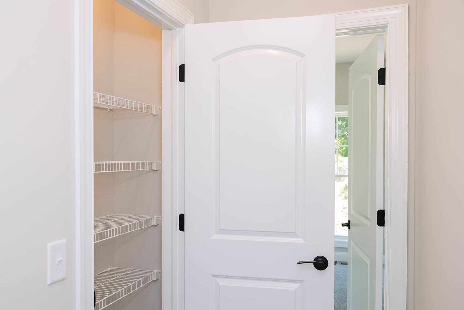 White paneled door with matte black handle and black hinges, adjacent to a white wire shelf mounted on a closet wall