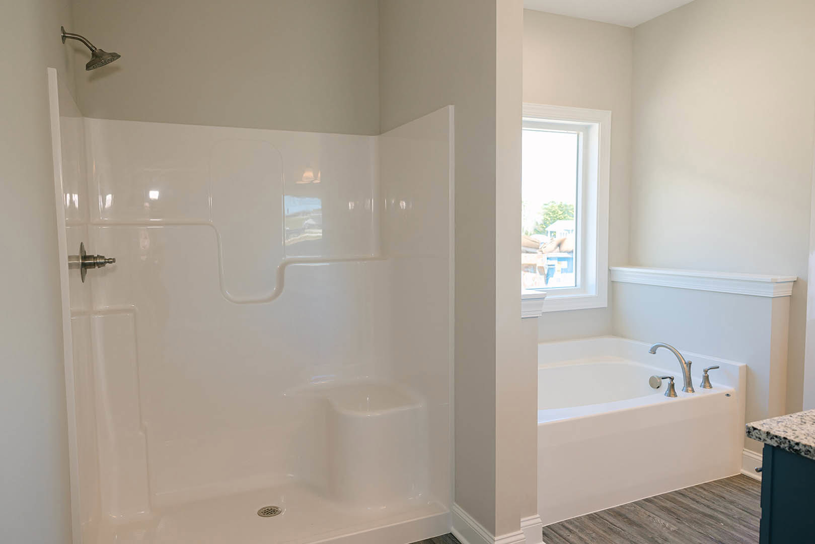 Bathroom featuring a freestanding white bathtub with chrome faucets, glass-enclosed tile shower, wood flooring, and a window overlooking the exterior of the house
