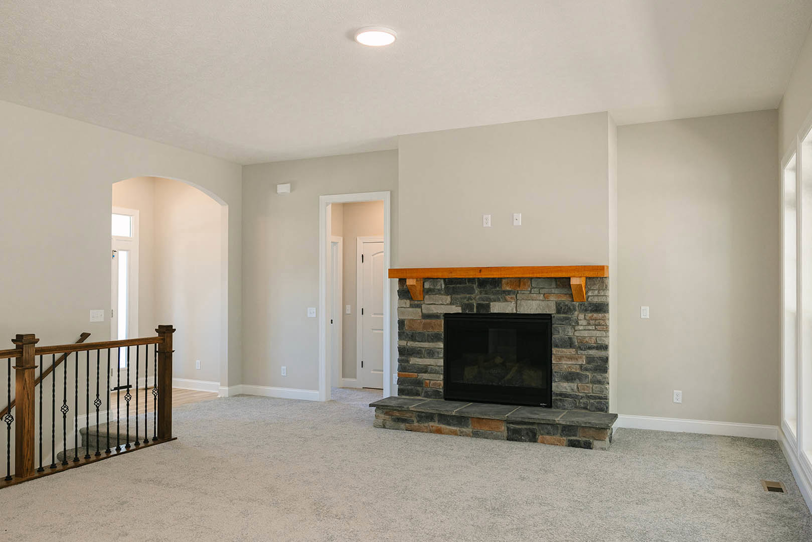 Stone fireplace with glass door and wood beam mantel, white plaster walls, hardwood flooring, ceiling light, and white door in a modern living room.