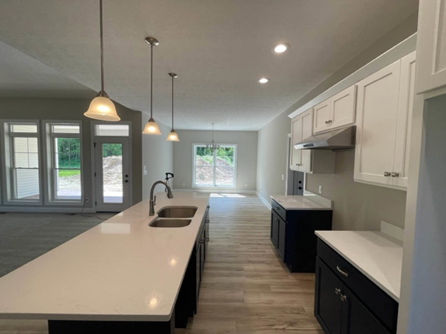 Spacious kitchen featuring a large white island with double sink, tile backsplash, white cabinetry, pendant lighting, and window above the counter.