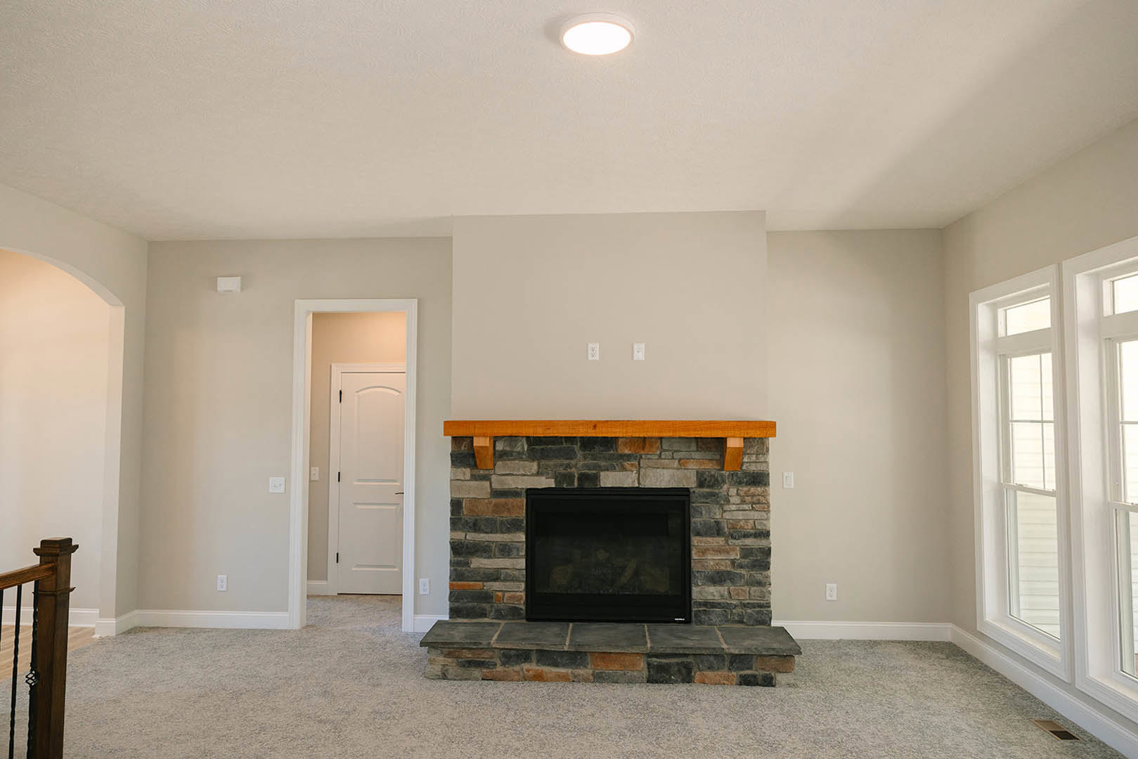Black-framed fireplace with wood mantel shelf, white plaster wall, exposed wood beam, close-up wooden post, and white door with black handle in a den.