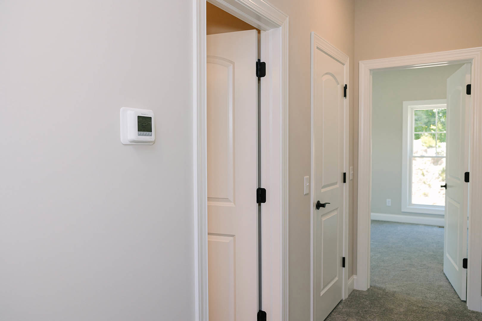 White paneled door with glass window, digital wall-mounted screen, light-colored flooring, and smooth white walls in a modern interior hallway