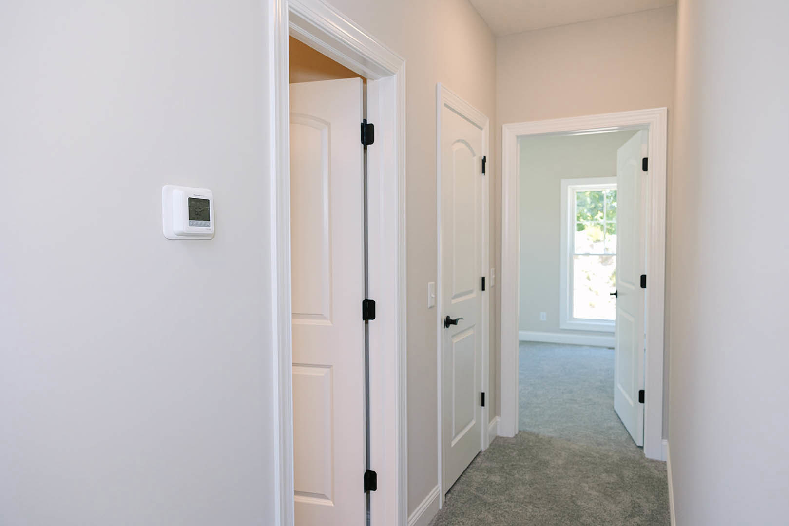 Hallway with white paneled doors, white walls, light wood flooring, and a digital thermostat mounted near a door with a frosted glass window