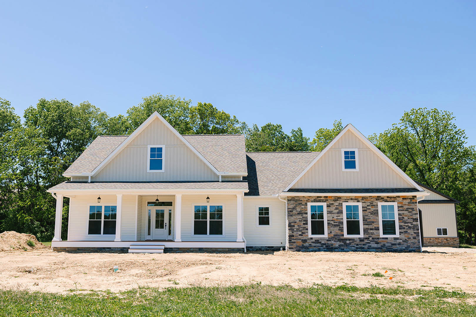 Stone and brick exterior home with white-framed windows featuring blue panes, surrounded by dirt landscaping and mature trees in the background
