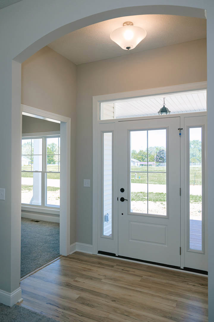 White door with glass panes opening onto wood flooring, ceiling light fixture overhead, view of green lawn through doorway